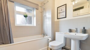 Un baño con bañera, inodoro, lavabo y una ventana con una planta.