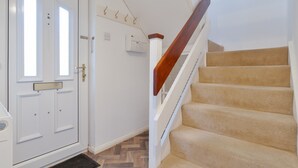 A white door with a brass handle, a wooden staircase with beige carpeted steps, and a white wall with a thermostat and hooks.