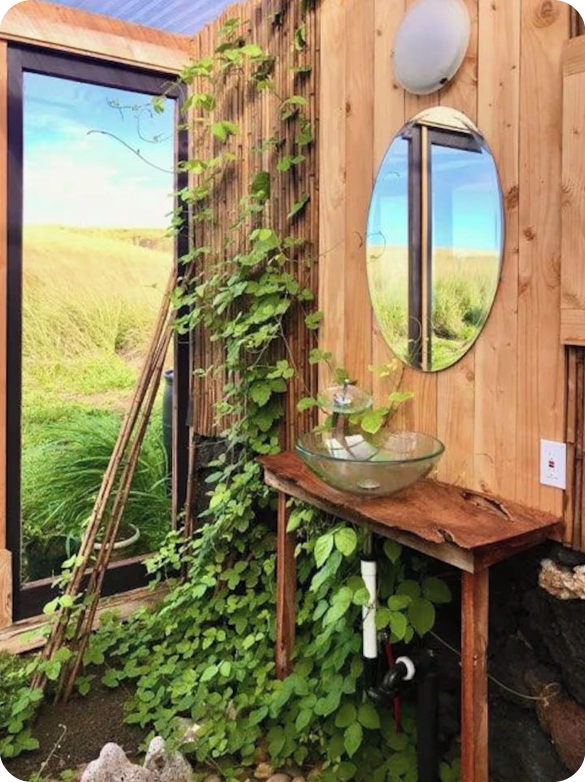 Una cabaña rústica de madera con puerta de vidrio, un banco de madera con un cuenco de vidrio y un espejo en la pared.