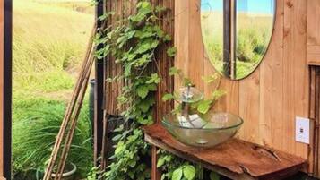 Una cabaña rústica de madera con puerta de vidrio, un banco de madera con un cuenco de vidrio y un espejo en la pared.