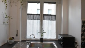 Une cuisine équipée d’un évier à deux bacs, d’un four à micro-ondes, d’une plante en pot et d’une fenêtre ornée de rideaux légers.