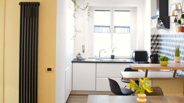 Une cuisine moderne avec des meubles blancs, un radiateur noir et un coin repas comprenant une table et des chaises.