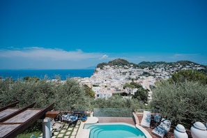 A pool area with lounge chairs and a view of a coastal town.