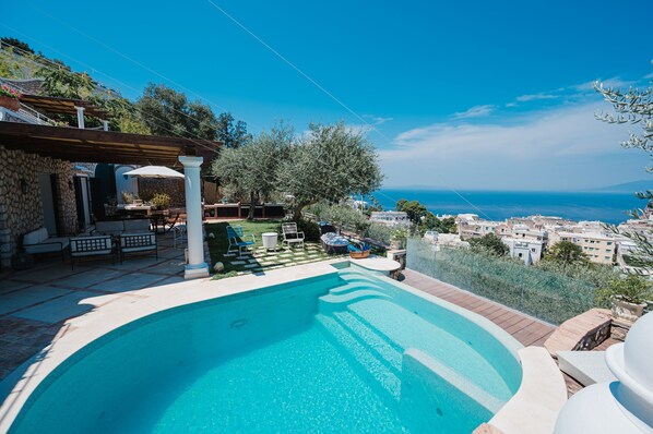 Una piscina con vistas al mar, mobiliario exterior y un edificio de piedra.
