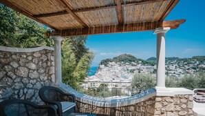 A terrace with stone walls, wicker furniture, and a view of a coastal town. - Villa Pietraserena by Elite Villas (Capri)