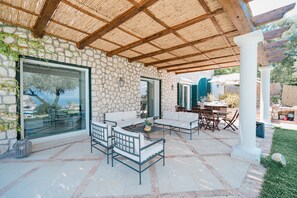Un patio al aire libre con muros de piedra, una pérgola de madera y mobiliario exterior.