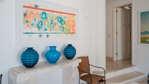 A room with a fireplace, two blue vases, a colorful abstract painting, and a wicker chair. - Villa Pietraserena by Elite Villas (Capri)