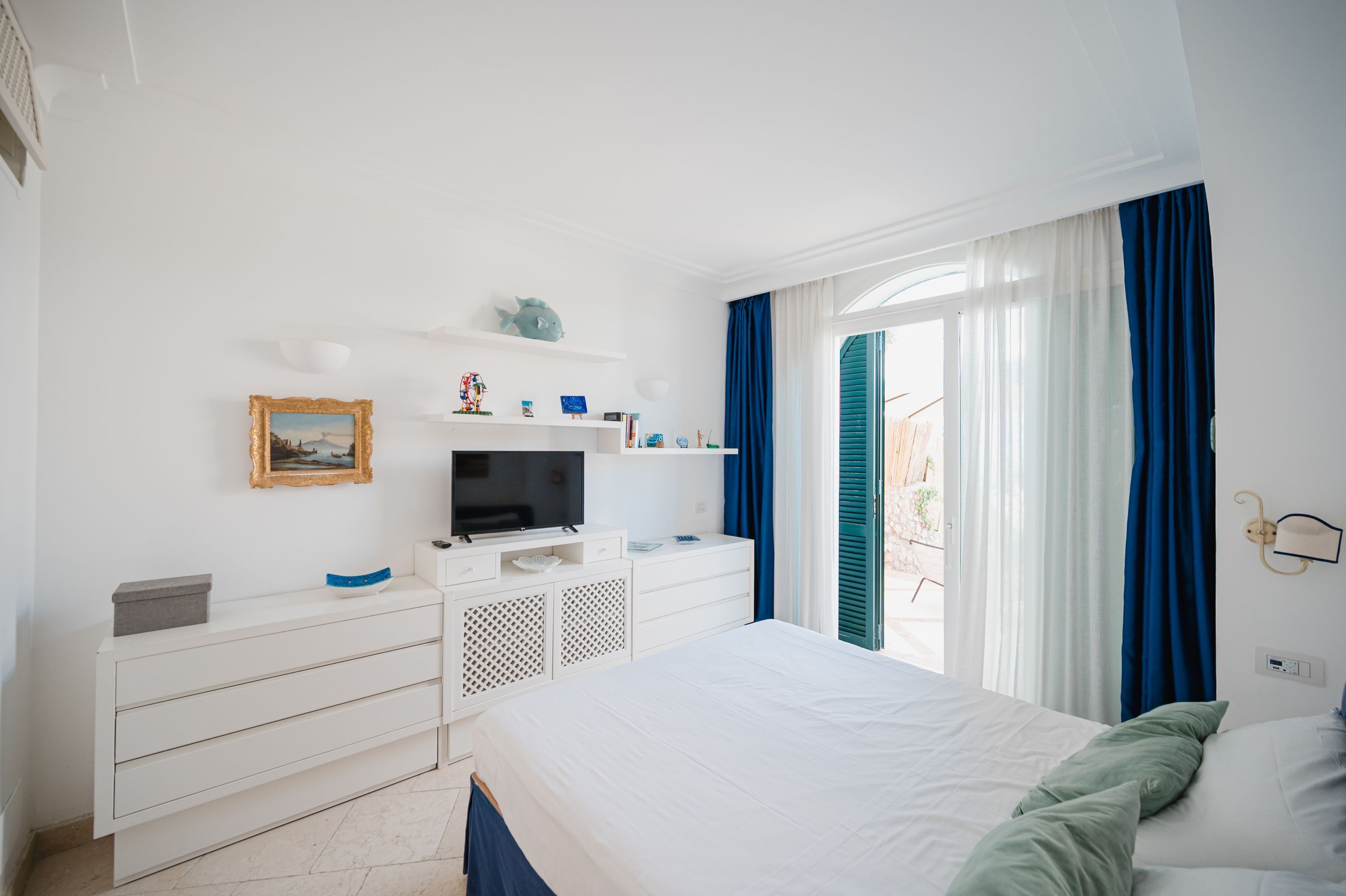 A bedroom with a bed, a TV, a dresser, and a window with curtains.