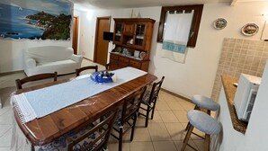 A dining area with a wooden table, chairs, a white sofa, and a cabinet with glass doors. - Villa Eden 2' Sea + Free Parking (Sardegna)