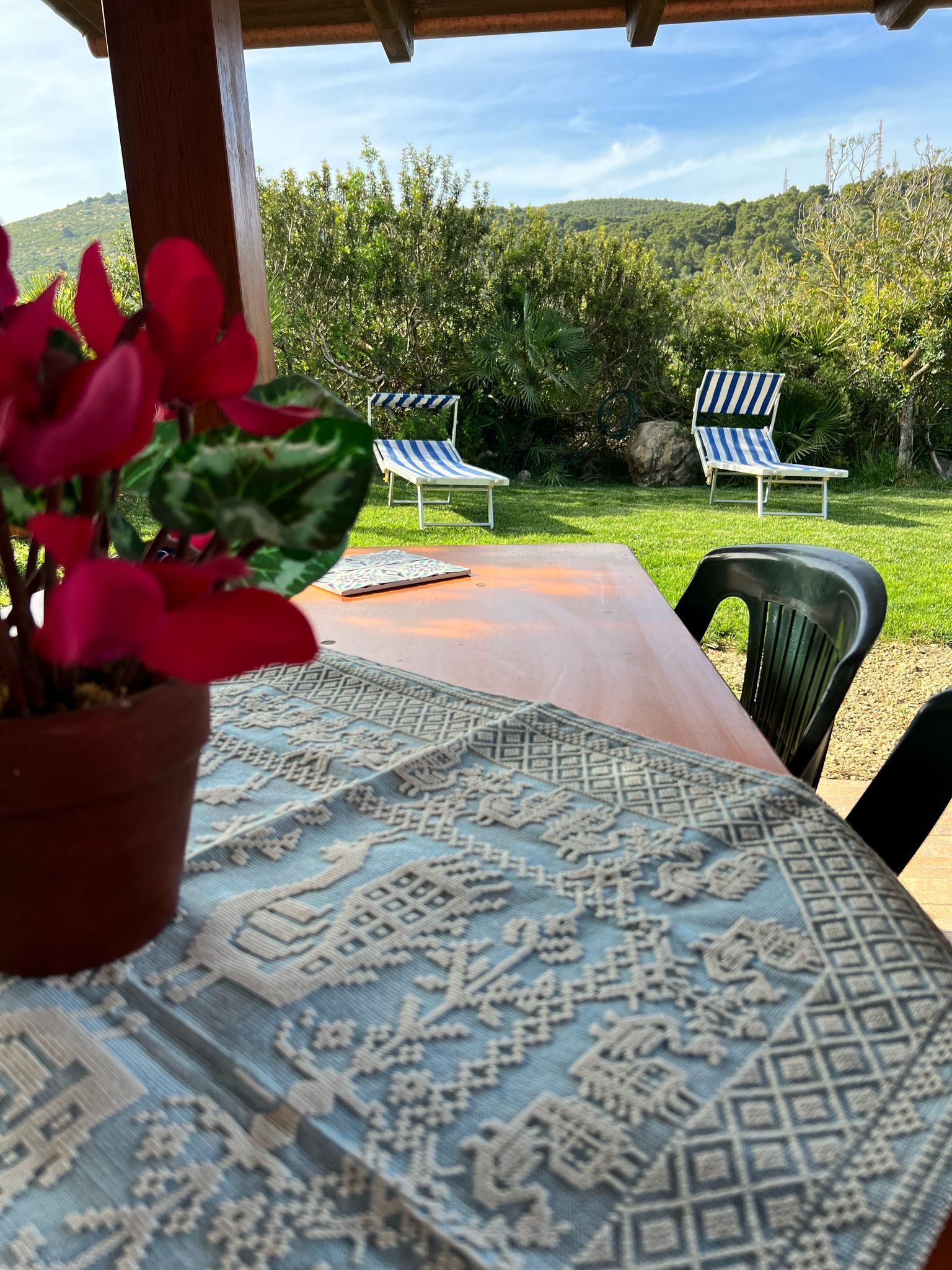 A covered outdoor seating area with a patterned tablecloth, two striped lounge chairs, and a potted plant.