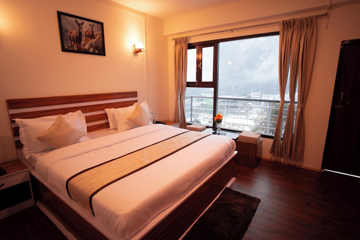 A large bed with a wooden headboard, a nightstand, a bedside table, and a window with curtains.