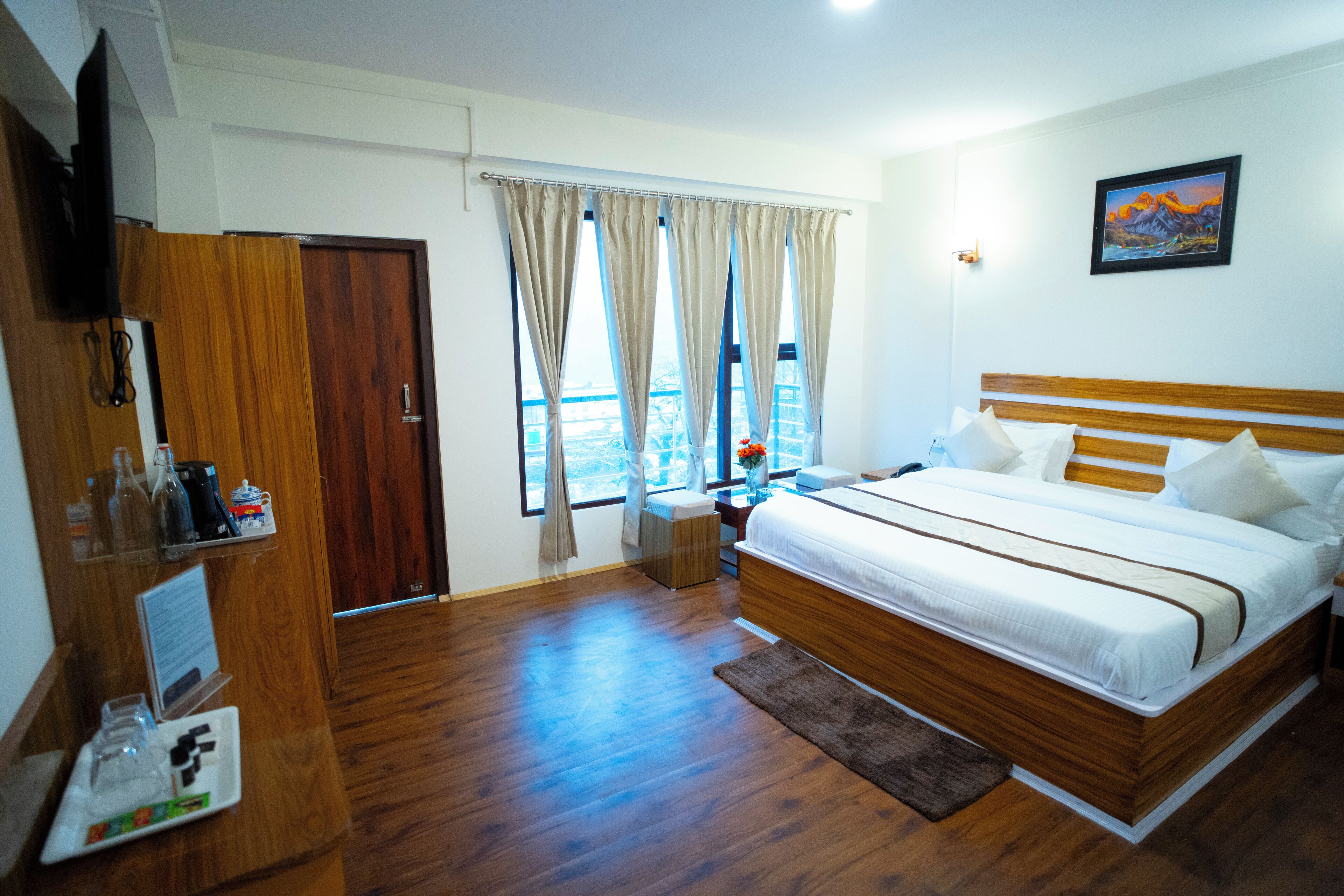 A hotel room with a wooden bed, a TV, a window with curtains, and a painting on the wall.