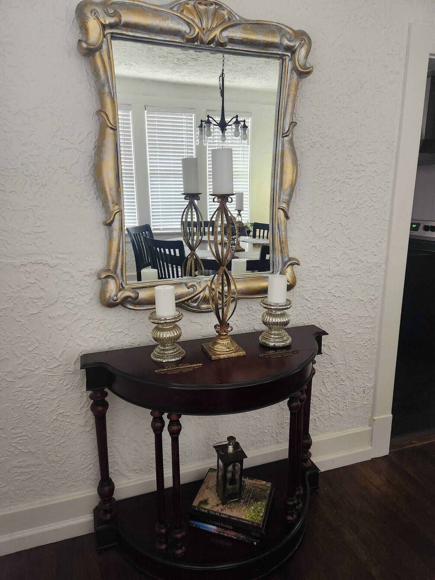 A dark wooden console table with a mirror above it, a chandelier, and two candle holders.