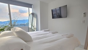 Une chambre moderne avec un grand lit, un téléviseur à écran plat et une vue sur le paysage urbain par la fenêtre.