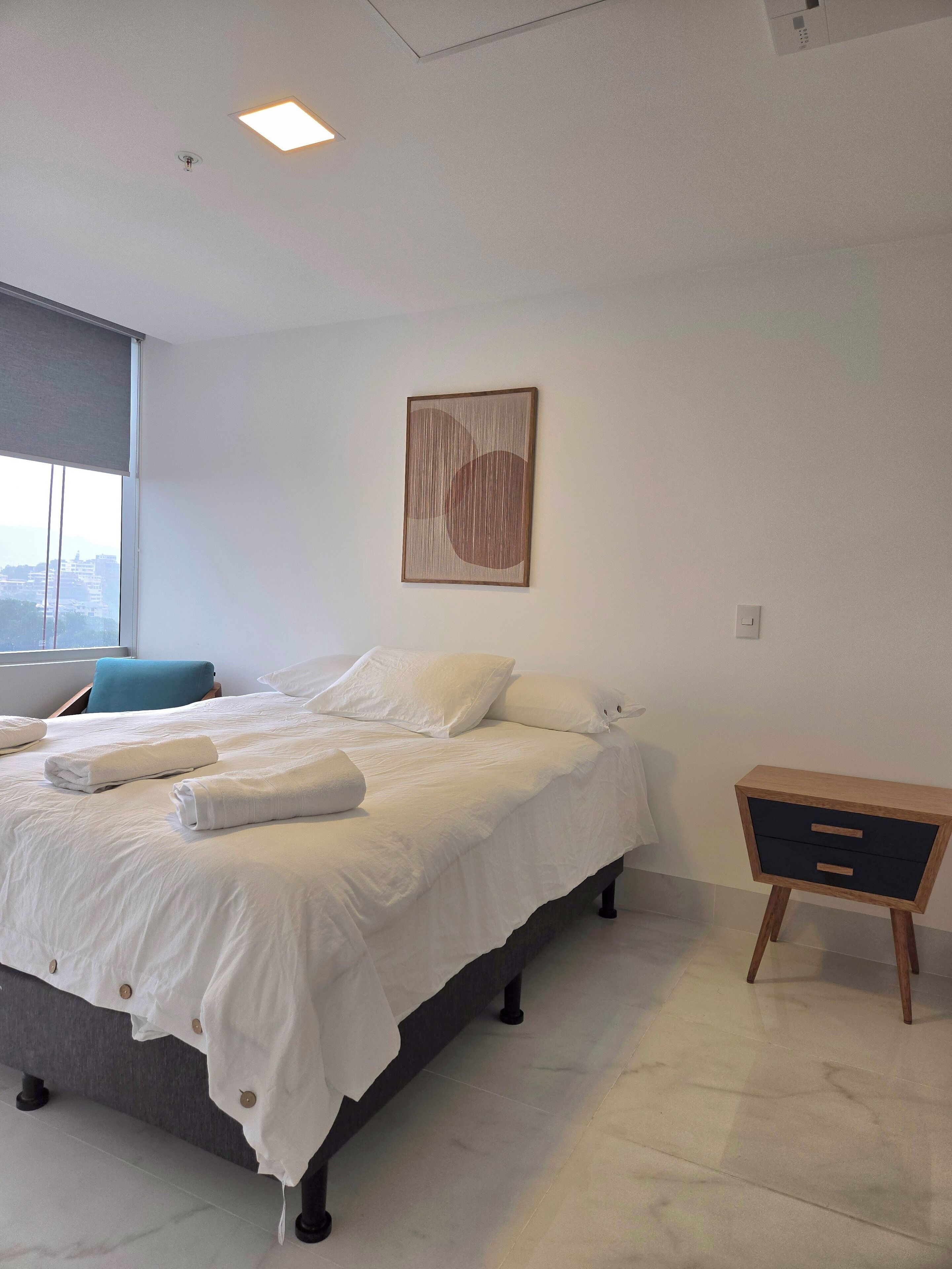 Une chambre à coucher moderne avec un lit, des oreillers, une table de chevet et une œuvre d’art accrochée au mur.