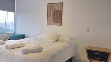 Une chambre à coucher moderne avec un lit, des oreillers, une table de chevet et une œuvre d’art accrochée au mur.