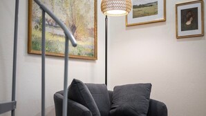 Moderni olohuone, jossa on harmaa sohva, lattiavalaisin ja seinällä taideteoksia.