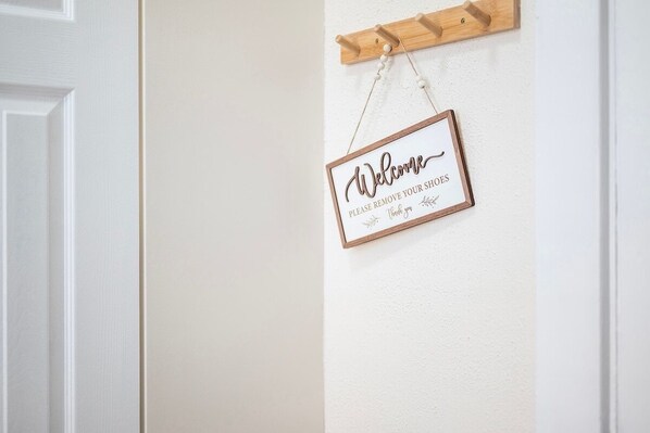 Une pancarte d’accueil indiquant qu’il faut enlever ses chaussures, fixée au mur, avec un porte-chaussures en bois juste au-dessus.