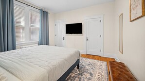 A bedroom with a bed, a TV mounted on the wall, and a window with curtains. - Modern 1 Bdr Apt unit#2 Sleeps4 (Pittsburgh)