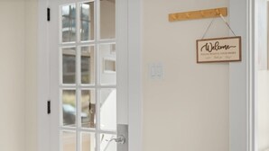 A white door with a glass panel, a wooden sign saying "Welcome Please Remove Your Shoes", and a light switch on the wall.