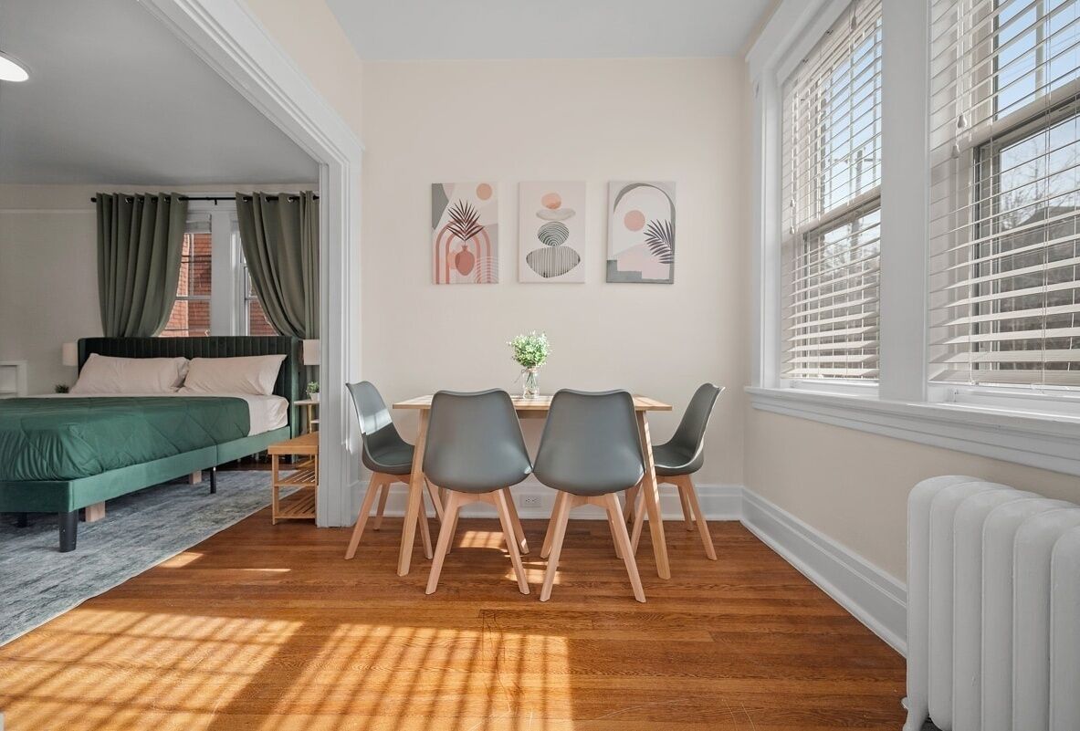 Um quarto com uma cama, uma mesa de jantar com cadeiras, um radiador e obras de arte na parede.