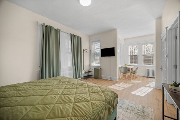 Une chambre à coucher avec un lit matelassé vert, un bureau avec une chaise et un téléviseur fixé au mur.