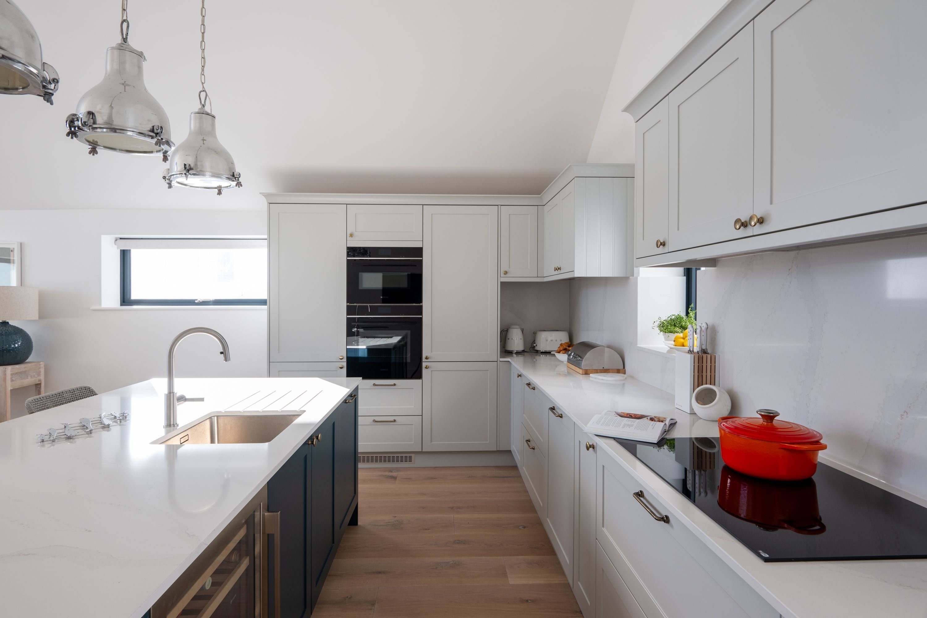 Une cuisine moderne avec des meubles blancs, un évier en acier inoxydable et une plaque de cuisson noire.