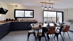 A modern kitchen with dark cabinetry, a wooden countertop, and a dining area with a large table and chairs.