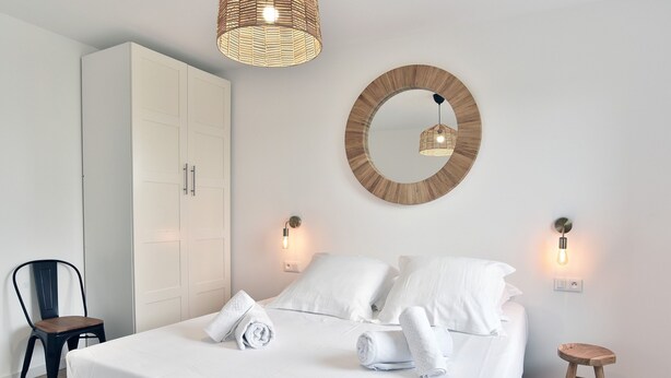 A neatly arranged bedroom with a bed, a wardrobe, a chair, and a stool.