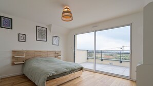 A modern bedroom with a wooden bed, large windows, and artwork on the walls.