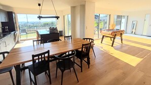 A modern kitchen with a dining area, a foosball table, and large sliding glass doors leading to a balcony with a view.