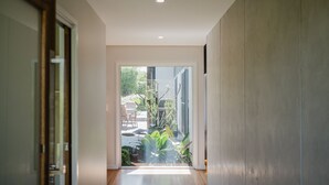 A hallway with a glass door leading to an outdoor area with plants and a patio. - The Magic Beach House (Narrawallee)