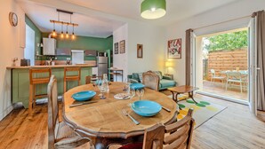 A dining area with a wooden table and chairs, a kitchen in the background, and a sliding glass door leading to an outdoor patio. - Le 52 - Proche du GR34 (Morlaix)