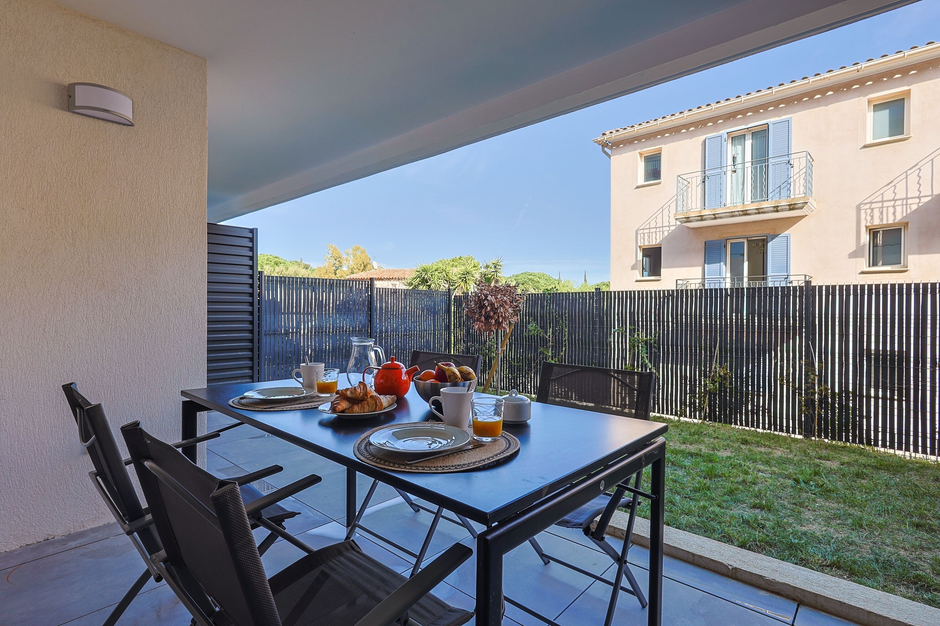 Eine Terrassensitzgelegenheit im Freien mit einem Tisch, gedeckt für ein Frühstück, mit Croissants, einem Teekessel und Orangensaft.