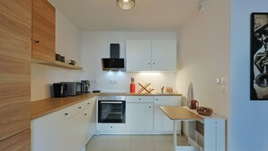 A modern kitchen with white cabinets, a wooden countertop, a built-in oven, and a small dining table. - Casa Kenez - A 5min de la plage (Cavalaire-sur-Mer)