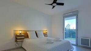 A bedroom with a bed, bedside lamps, a ceiling fan, and a view through a sliding door. - Casa Kenez - A 5min de la plage (Cavalaire-sur-Mer)