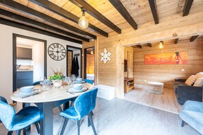 Un interior moderno con techo de madera, zona de comedor con sillas azules, una mesa redonda y un sofá al fondo.