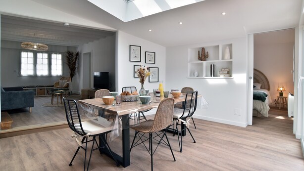 A spacious living area with a high ceiling and skylight, a dining table with chairs, and a cozy seating area with a sofa and chairs.