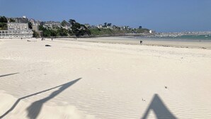 A sandy beach with a few people and a pier in the background.