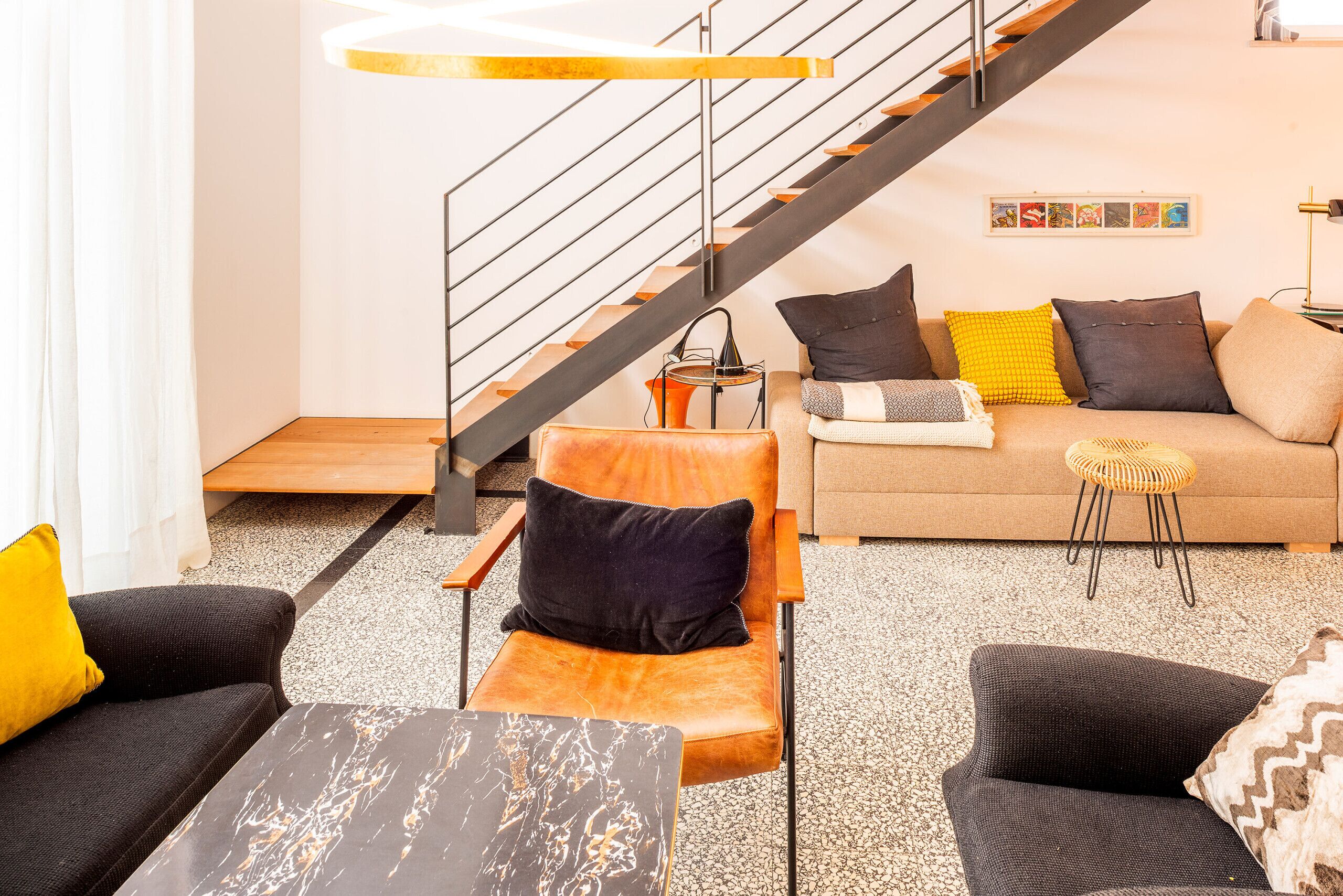 Un salon moderne avec un canapé, des fauteuils, une table basse et un escalier.