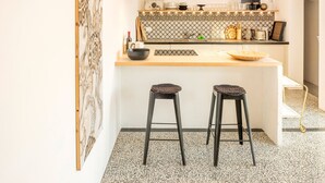 Una cocina con salpicadero de mármol, dos taburetes y una encimera con diversos utensilios de cocina.