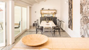 Un comedor con una mesa grande, sillas y un cuenco decorativo. Se ve una zona de cocina con armarios y una encimera al fondo.