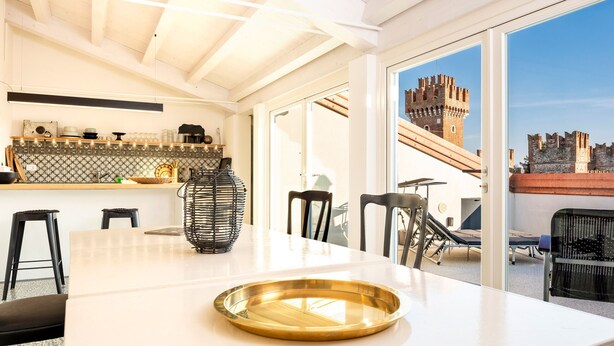 Una cocina moderna con una isla grande, un comedor con sillas y vista a un castillo a través de una puerta de vidrio.