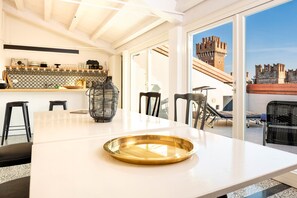 A modern kitchen with a large island, a dining area with chairs, and a view of a castle through a glass door. - 617A Lakeview Apartment Cristina (Lazise)