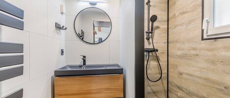 Une salle de bain moderne avec un mur d’accent en bois, un miroir rond, un lavabo avec un robinet et un espace douche.
