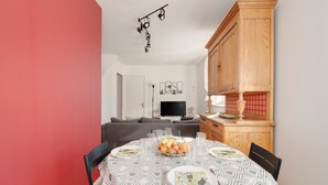 A dining area with a round table set for four, a fruit bowl, and a television in the background. - Aux 4 saisons - Proche de Gérardmer (Corcieux)