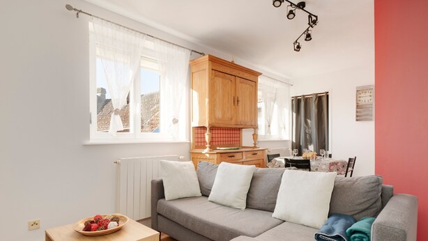 A cozy living room with a grey sofa, wooden cabinet, and a small table with a bowl of fruit. - Aux 4 saisons - Proche de Gérardmer (Corcieux)