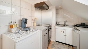 A compact kitchen with white cabinets, a built-in oven, a coffee machine, and a sink. - Aux 4 saisons - Proche de Gérardmer (Corcieux)