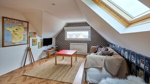 Une chambre à coucher aménagée dans un espace sous les toits, avec un plafond en pente, une lucarne, un lit, un bureau et une carte accrochée au mur.