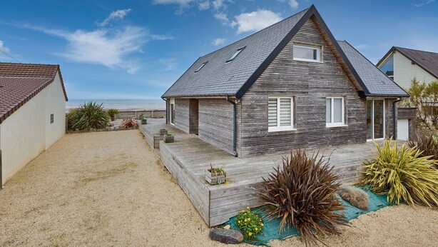 Une maison moderne avec un toit en pente, une terrasse en bois et une allée gravillonnée.